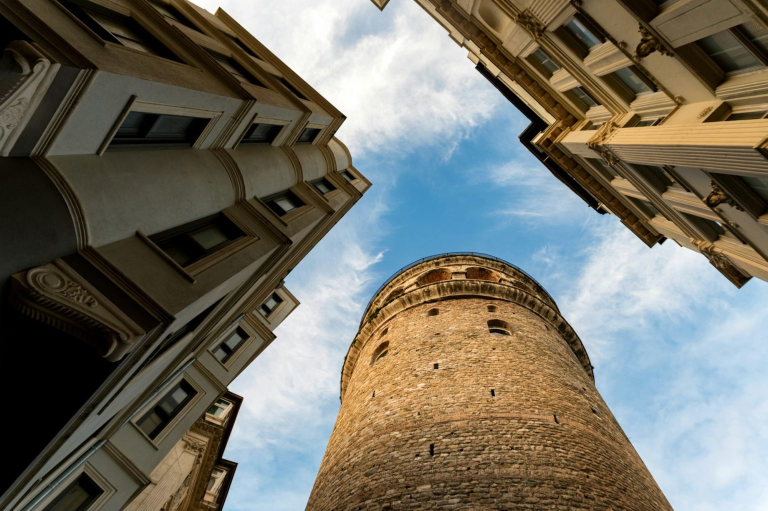 View of Galata Tower from below surrounded by classic buildings against blue sky
